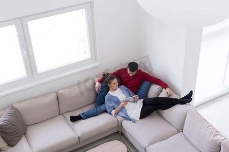 老婆摄影照片_年轻夫妇在家里用平板电脑放松，在客厅的沙发上看书。
