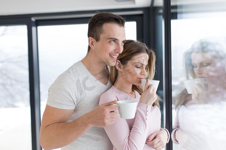 在寒冷的冬日里，浪漫幸福的年轻夫妇在家中靠窗喝着早晨的咖啡