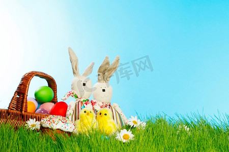 白色兔子摄影照片_绿色草地上有彩蛋和兔子的复活节篮子，上面有鲜花。草地上的复活节篮子