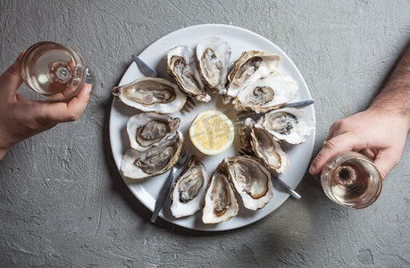 美味的菜肴摄影照片_美味的牡蛎配上一片柠檬和一杯白葡萄酒，俯瞰。异国情调的菜肴--酒生蚝