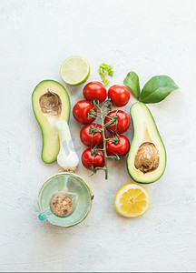 新鲜沙拉成分：半鳄梨，西红柿，柠檬和橄榄油在白色背景。俯视图。素食。健康饮食