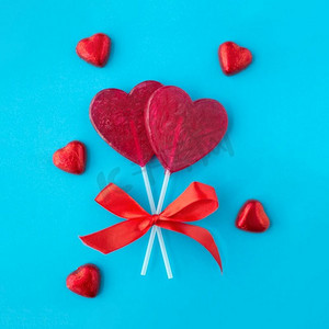 情人节浪漫蓝色摄影照片_情人节，糖果和浪漫概念—红色心脏形状棒棒糖在蓝色背景情人节红心棒棒糖