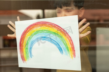 鼓舞人心的小孩子拿着彩虹的画通过窗口 