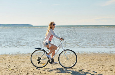 人，休闲，生活理念-快乐的年轻女子骑着自行车沿着夏日海滩。快乐的女人骑着自行车沿着夏日海滩