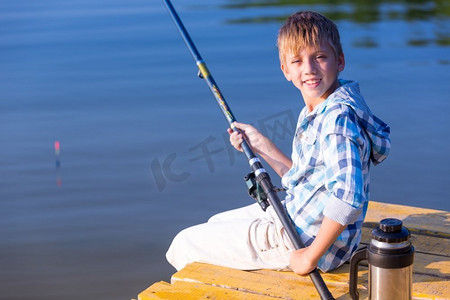 男孩在蓝色衬衫坐在码头与钓竿由海
