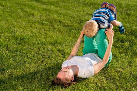 草地玩的孩子摄影照片_快乐的女人和孩子在草地上玩得很开心。公园里母子俩在绿茵茵的草地上休息的家庭生活场景。