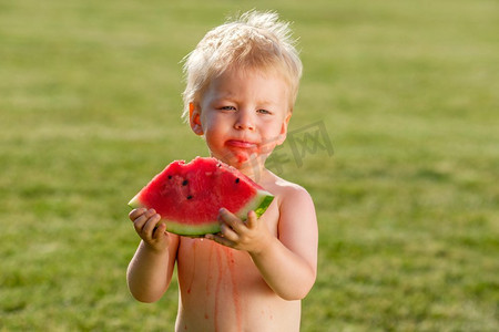 户外蹒跚学步的孩子的肖像。一岁的男婴在花园里吃西瓜片的农村场景。快乐的孩子肮脏的脸。