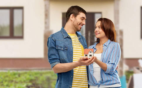 房地产，家庭和抵押概念—微笑的夫妇持有房子模型在家背景微笑的夫妇举行房子模型
