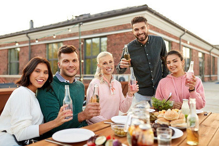 休闲和人的概念-快乐的朋友在屋顶上喝酒，烧烤或晚宴。在屋顶上喝酒或参加烧烤派对的快乐朋友