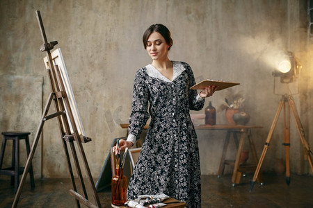 用画笔和调色板的女画家在艺术工作室画画.豹纹装吊带睡衣
