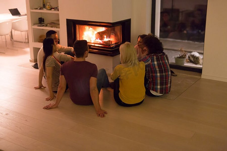 在寒冷的冬夜，一群年轻的多民族夫妇坐在壁炉前的地板上