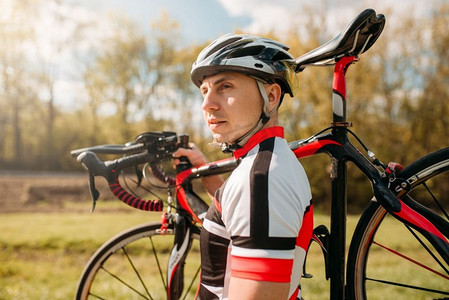 骑车人摄影照片_骑自行车的人戴着头盔和运动服，把自行车放在肩上，在柏油路上骑自行车。男运动员骑自行车。在自行车道上锻炼