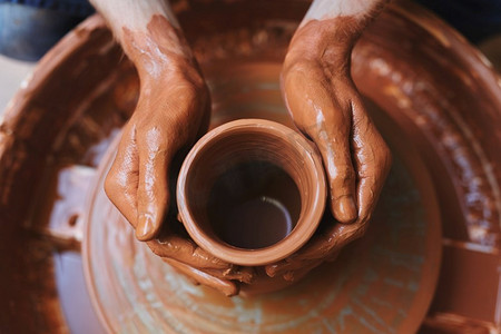 陶工在旋转陶罐上的脏手。未完成的壶