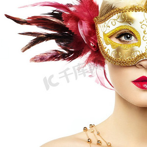 戴着神秘金色威尼斯面具的美丽年轻女子。时尚照片。红色羽毛面具