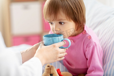 医疗保健、医学和人的概念—医生在家里给生病的小女孩喝热茶。医生在床上给生病的小女孩热茶