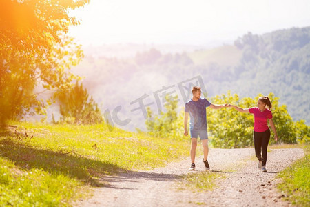 年轻幸福的夫妇享受着健康的生活方式，在乡村小路上慢跑穿过美丽的阳光森林，锻炼和健身的概念