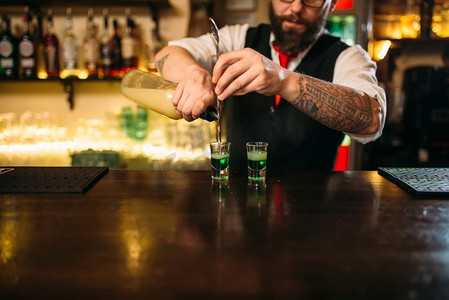 混合酒精饮料摄影照片_酒吧老板倒酒在玻璃后面的餐厅酒吧柜台。酒保倒酒精饮料在玻璃