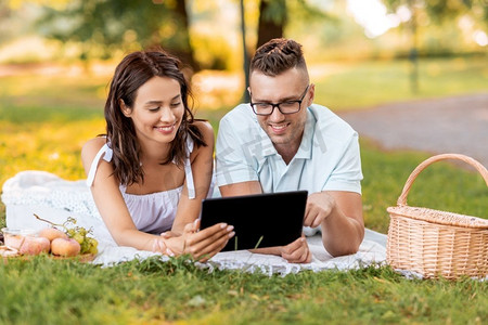 休闲与人概念—快乐夫妇与平板电脑电脑在夏季公园野餐。愉快的夫妇与平板电脑在野餐在公园