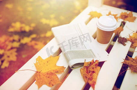 外卖摄影照片_季节和新闻概念秋季公园长椅上的报纸和咖啡杯。秋季公园长凳上的报纸和咖啡杯