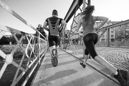 情侣慢跑摄影照片_城市运动，阳光明媚的早晨，健康的年轻夫妇在城市中慢跑过桥