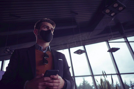 商人戴着冠状病毒防护医用口罩，同时使用智能手机和新常态智能技术