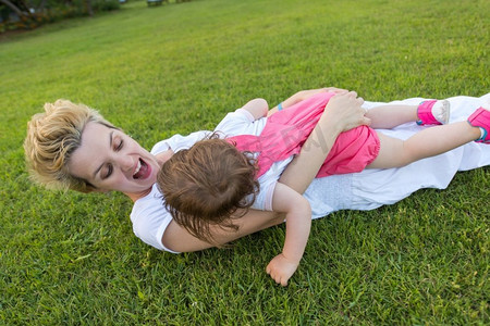 年轻的妈妈和可爱的小女儿在后院的草地上享受着自由的时光，大自然中的幸福家庭概念