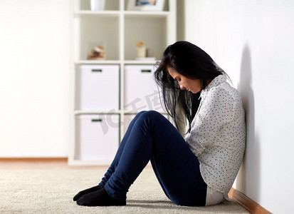 人、悲伤和家庭暴力的概念--不快乐的女人坐在地板上哭在家里。不开心的女人在家里的地板上哭