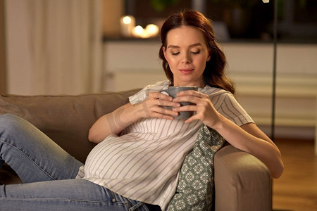 怀孕和人的概念—孕妇喝茶在沙发上在家里。孕妇在家喝茶