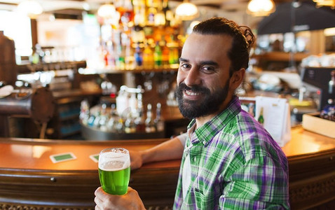 人，休闲和圣帕特里克节的概念-在酒吧或酒吧喝绿啤酒的快乐男人。在酒吧或酒吧喝绿啤酒的男人