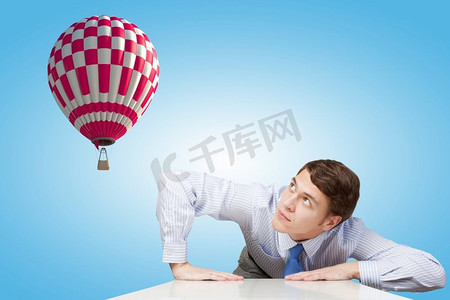 浮空器摄影照片_坐在飞天气球上的年轻人从桌子底下往外看。飞行浮空器