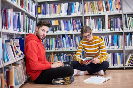 书笔记摄影照片_两个年轻的学生坐在学校图书馆里，用笔记本电脑做笔记，