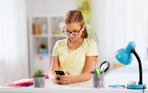 教育、科技与学习理念--学生女孩拿着智能手机在家做作业。拿着智能手机做作业的女学生
