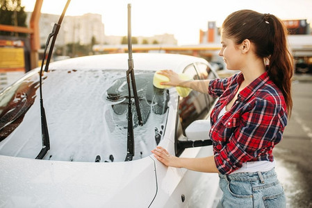 妇女自助洗车，洗车过程。夏季户外洗车用海绵清洁汽车前玻璃的女性