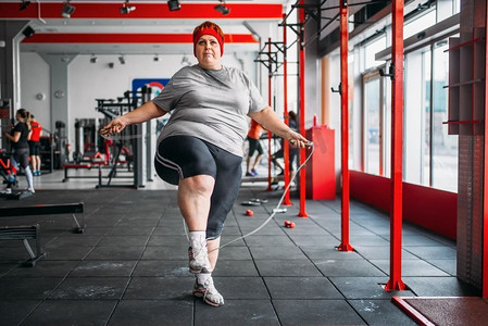 脂肪出汗的妇女做锻炼与绳子在体育馆。燃烧卡路里，肥胖女性在体育俱乐部训练，肥胖
