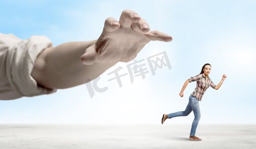 逃离摄影照片_一名女子从手中逃脱。穿着休闲的年轻女子逃离大手