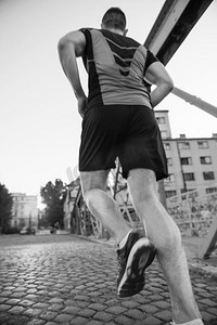 一个年轻的运动男子慢跑过桥在阳光明媚的早晨在城市