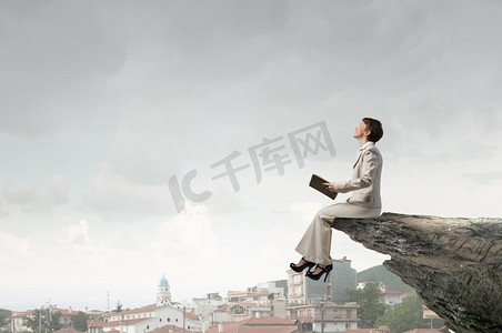 扩宽摄影照片_拿着书的女人。一名西装革履的成年女子坐在岩石边，手里拿着一本旧书