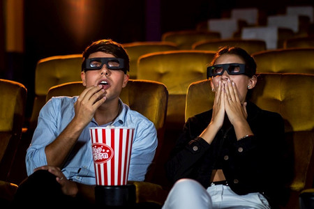 男人和女人在电影院看电影与3D眼镜。饶有兴趣地看着屏幕，兴奋地吃着爆米花，