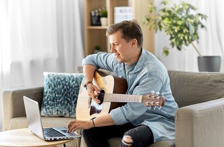 休闲，音乐和人的概念—年轻人或音乐家与笔记本电脑在家里弹吉他。年轻人与笔记本电脑弹吉他在家里