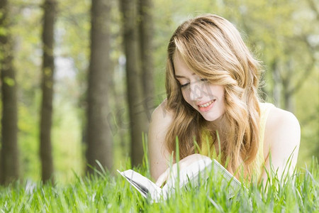 年轻的美女躺在草地上看书，春考概念，文案空间。女人躺在草地上看书