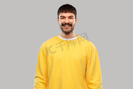 人们概念—微笑的年轻人在灰色背景的黄色运动衫。微笑的年轻人穿着黄色运动衫