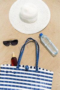 度假，旅行和夏季概念—沙滩袋，防晒霜，太阳镜和帽子在沙滩上。沙滩袋，防晒霜，太阳镜和帽子在沙滩上