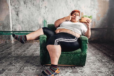 肥胖女性摄影照片_胖女人坐在椅子上吃三明治，超重，肥胖，暴食症。不健康的生活方式，肥胖