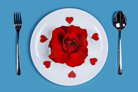 餐具设置盘玫瑰花和心在蓝色背景情人节浪漫晚餐概念。浪漫晚餐概念