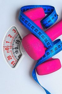 健康的生活方式健身减肥理念。特写粉红色哑铃与蓝色卷尺在白色规模