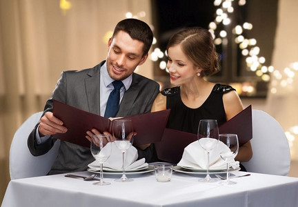 节日灯光摄影照片_约会、奢华和人们概念快乐的情侣在餐厅的菜单上，背景是节日灯光。与餐厅的菜单搭配
