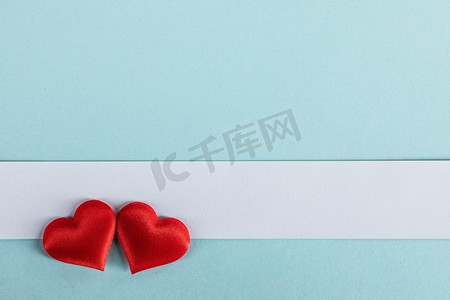 情人节两个红色丝绸心和白纸在蓝色纸背景，爱概念。’情人节红心在蓝色