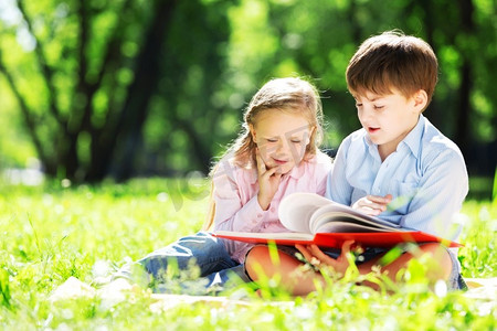 姐妹拉手摄影照片_姐姐和哥哥在公园里看书。夏季周末户外活动