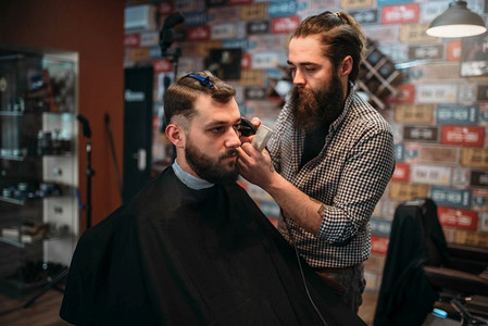 理发师剪头发的客户男子在黑色沙龙斗篷。理发店概念