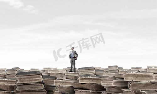 知识和教育是他的优势。年轻自信的商人，胳膊搭在腰上，站在一堆旧书上